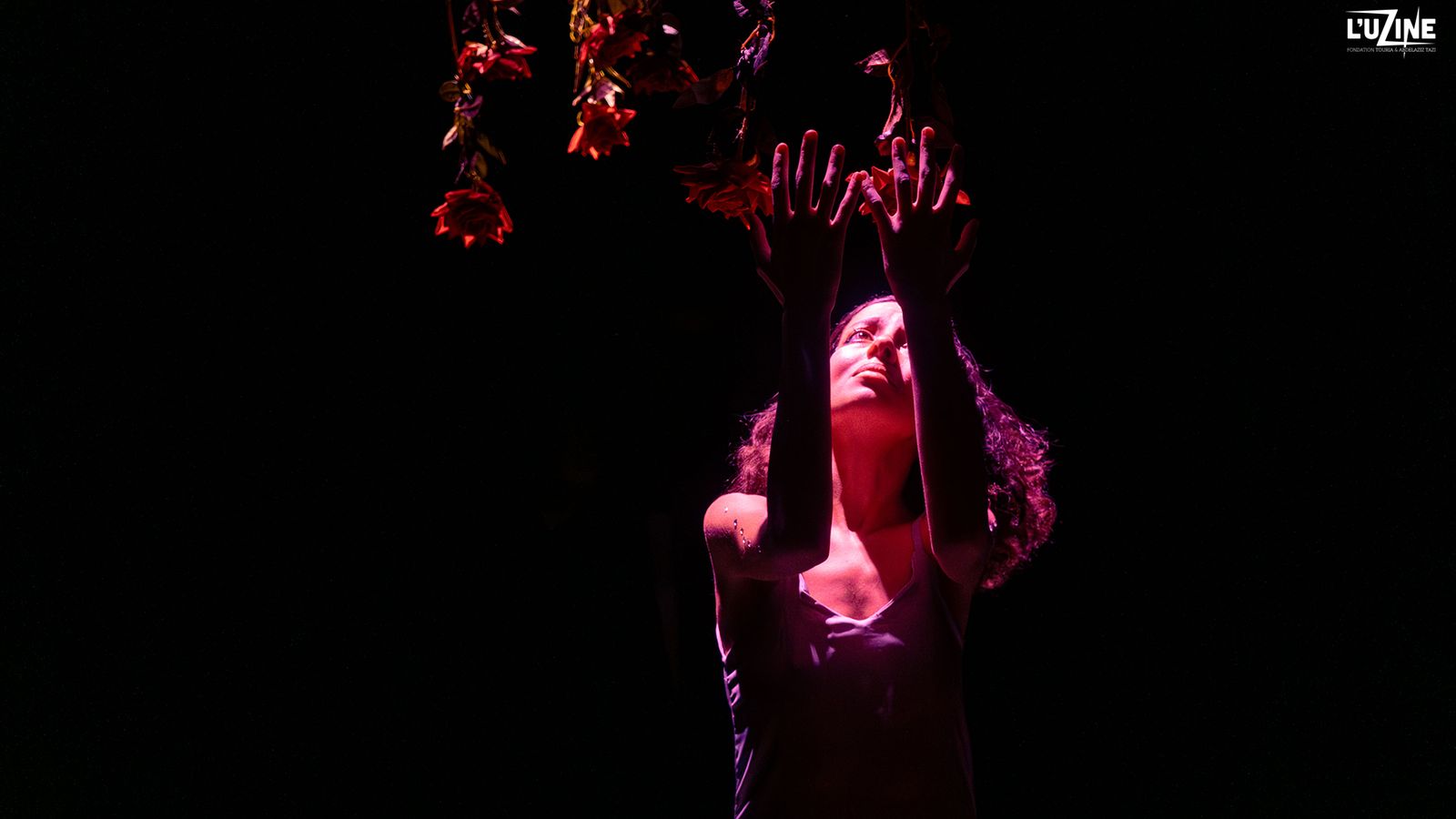 Dancer reaching toward hanging roses under stage light